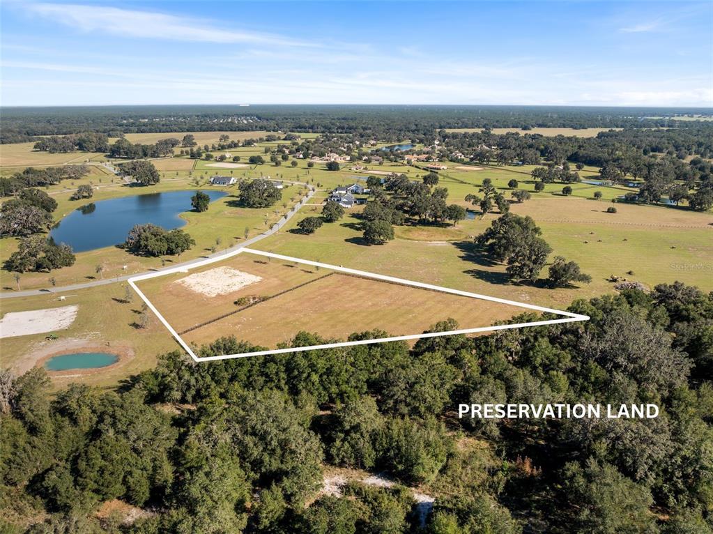 An aerial view shows a large, fenced grassy pasture surrounded by trees and a pond — 12793 SW 138TH LOOP, DUNNELLON, FL