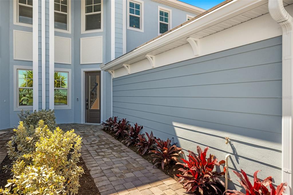 A paved walkway leads to the front entrance of a blue house with horizontal siding — 12785 JADE EMPRESS LOOP UNIT 202, VENICE, FL