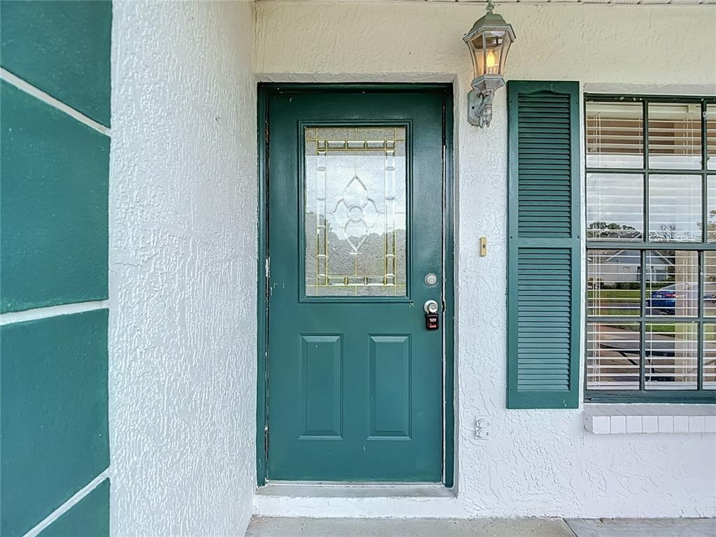 A green front door with a glass insert sits beside a window with green shutters — 11510 PAMPAS DRIVE, NEW PORT RICHEY, FL