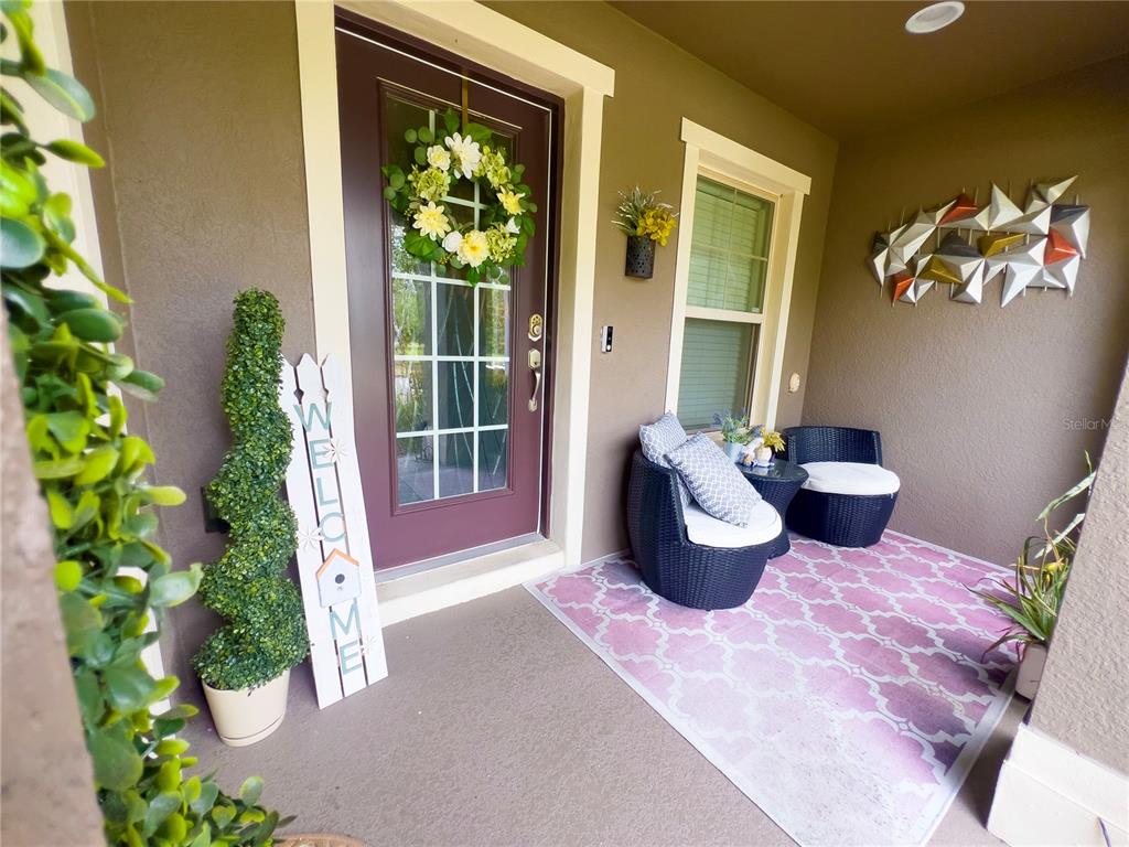 A covered front porch features a dark door, wicker chairs, and a patterned rug — 10730 SUNSET RIDGE LANE, ORLANDO, FL