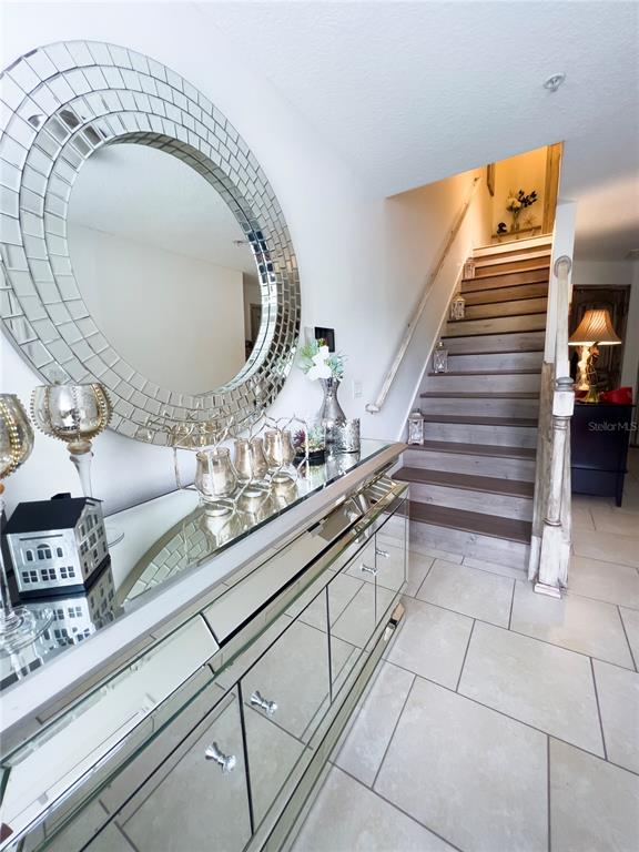 A mirrored console table and large circular mirror sit in a foyer with stairs — 10730 SUNSET RIDGE LANE, ORLANDO, FL