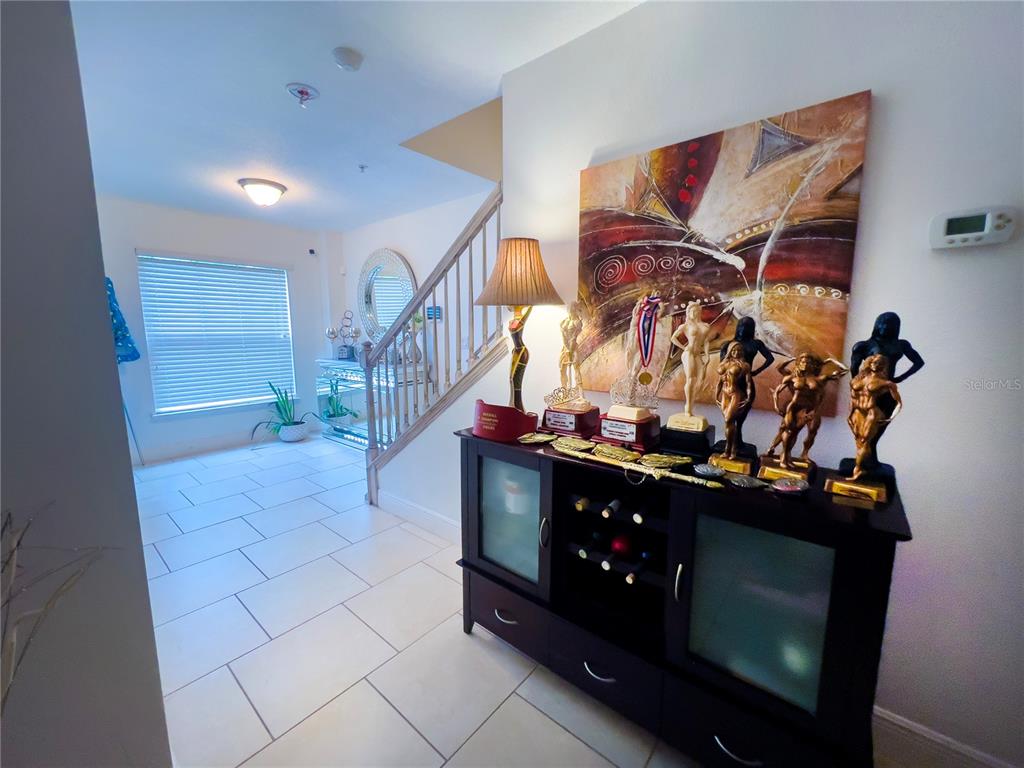 A foyer features a tiled floor, a staircase, and a cabinet displaying several trophies — 10730 SUNSET RIDGE LANE, ORLANDO, FL