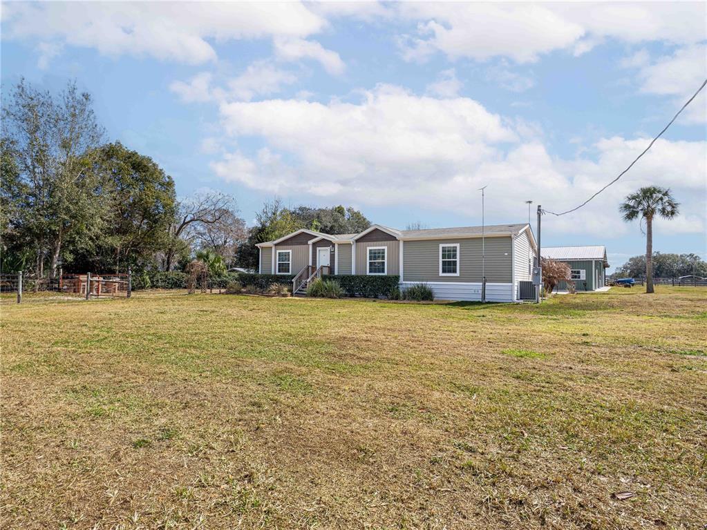 A single-story manufactured home sits on a large, grassy lot with a detached garage — 26444 COUNTY ROAD 44A, EUSTIS, FL