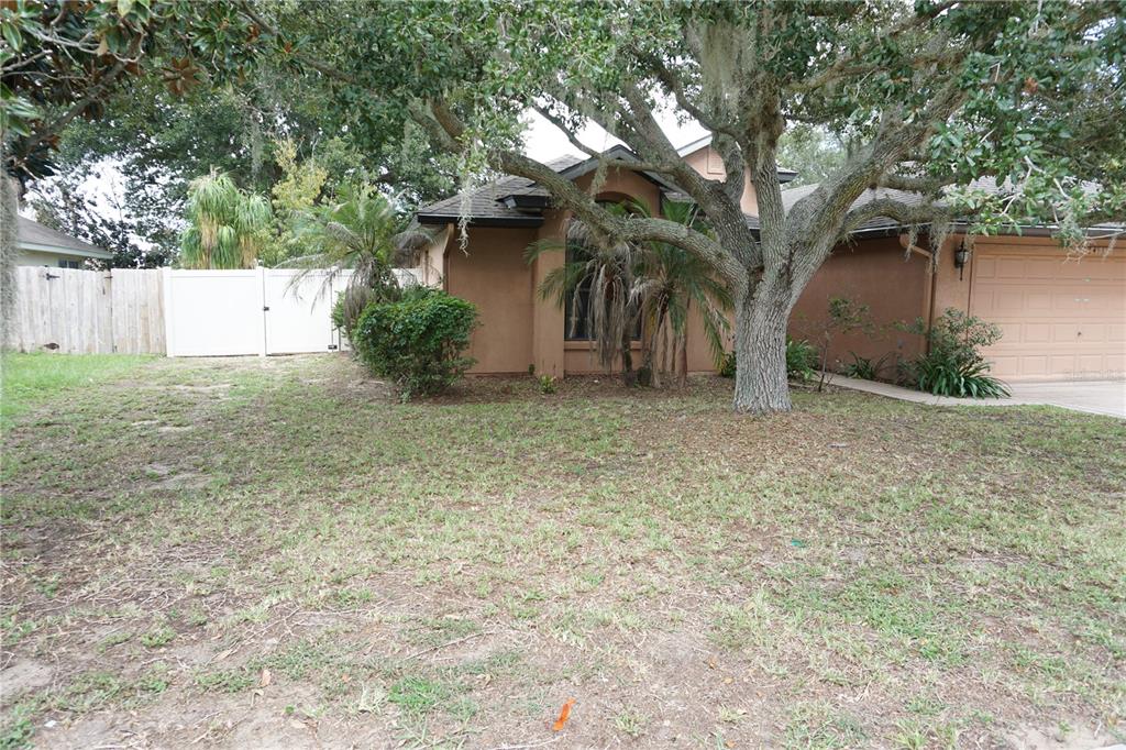 A single-story house with a tan stucco exterior, a two-car garage, and a large oak tree — 4531 TREASURE CAY ROAD, TAVARES, FL