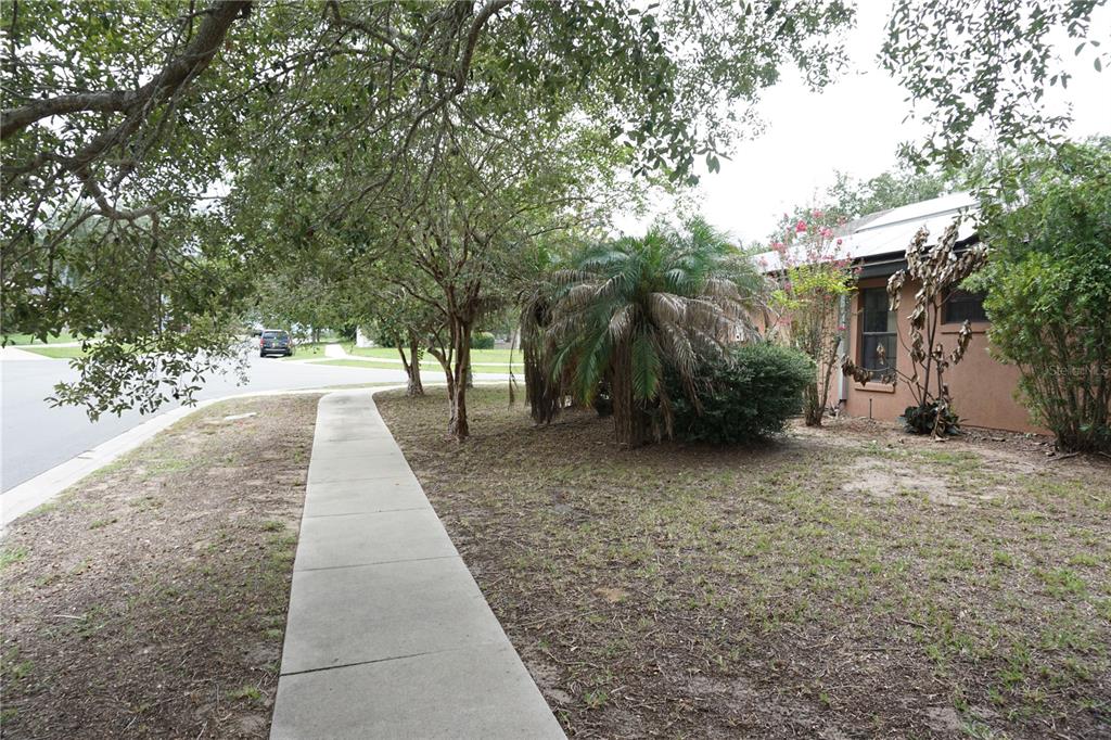 A sidewalk leads past trees and a palm tree toward the side of a house — 4531 TREASURE CAY ROAD, TAVARES, FL