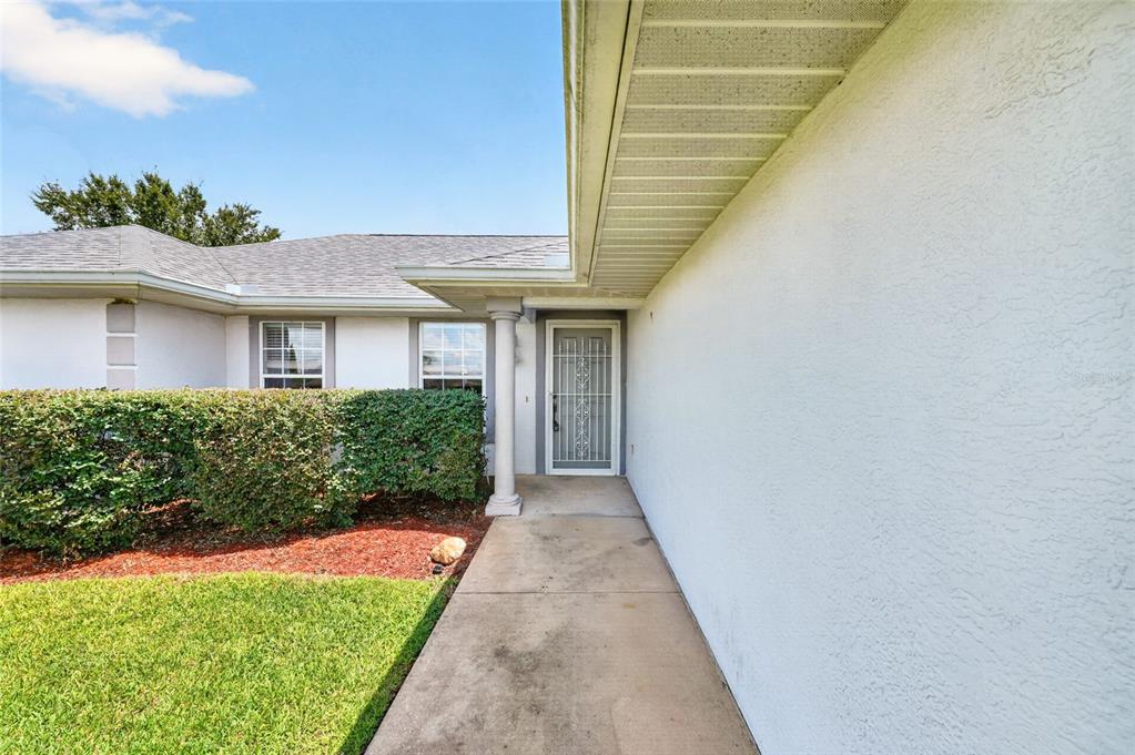 A concrete walkway leads to the front entrance of a house with white stucco walls — 17461 SE 110TH COURT, SUMMERFIELD, FL