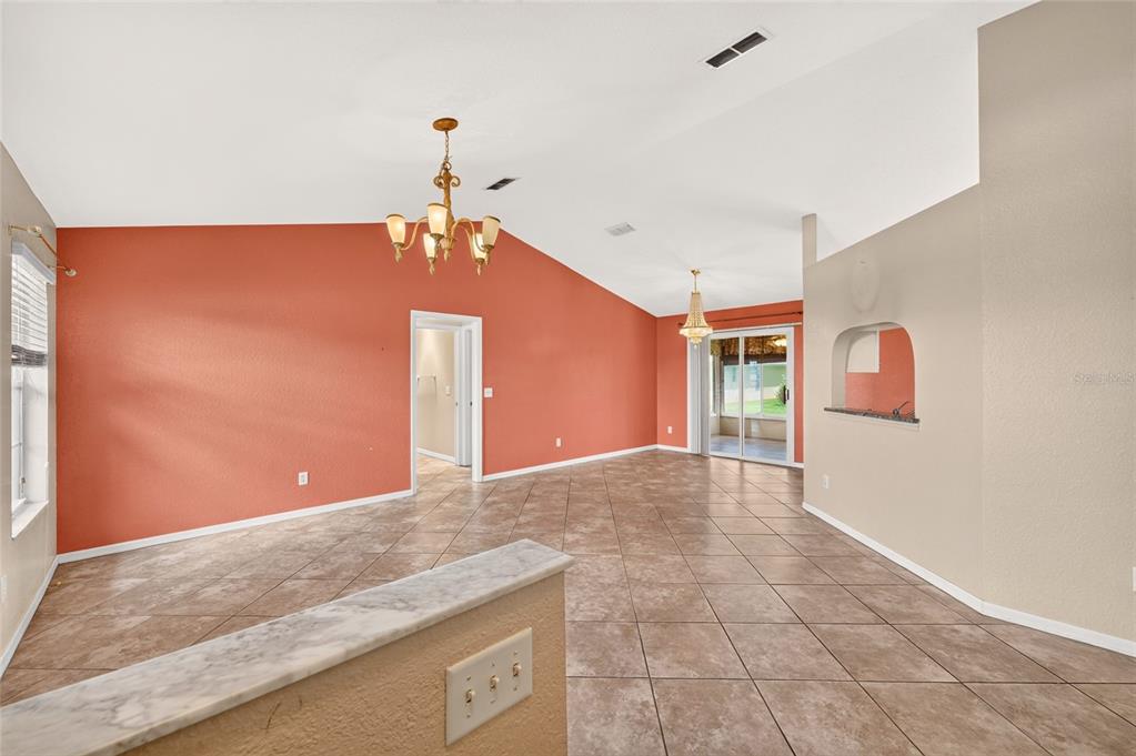 A living room with vaulted ceilings, terracotta-colored walls, tile flooring, and two hanging chandeliers — 17461 SE 110TH COURT, SUMMERFIELD, FL
