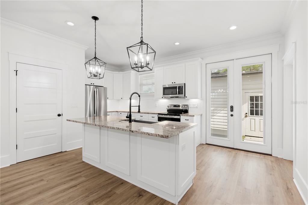 A white kitchen features a granite-topped island, stainless steel appliances, and wood-look flooring — 3923 W GRAY STREET, TAMPA, FL