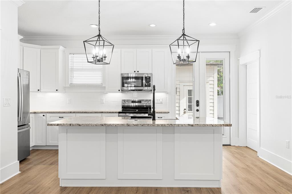 A white kitchen features a granite-topped island, stainless steel appliances, and two black pendant lights — 3923 W GRAY STREET, TAMPA, FL