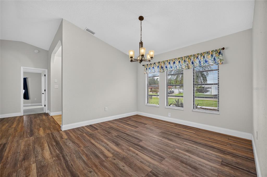 An empty dining room features wood-look flooring, a chandelier, and three windows with floral valances — 2058 LAKE VIEW BOULEVARD, PORT CHARLOTTE, FL