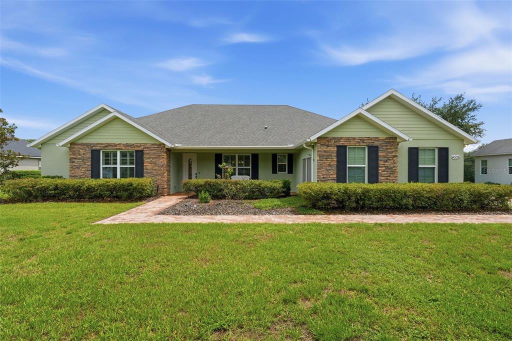 A single-story house with green siding, stone accents, and a paved walkway in the yard — 4526 CLAIRE ROSE COURT, MOUNT DORA, FL
