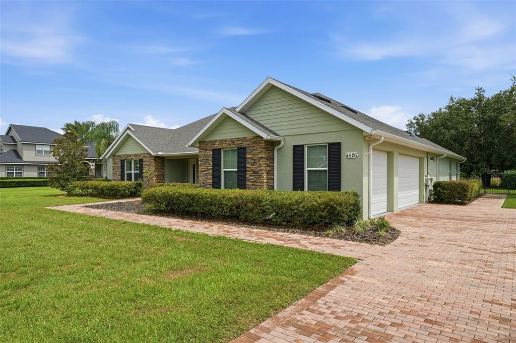 A single-story house with a green exterior, stone accents, and a brick paver driveway — 4526 CLAIRE ROSE COURT, MOUNT DORA, FL