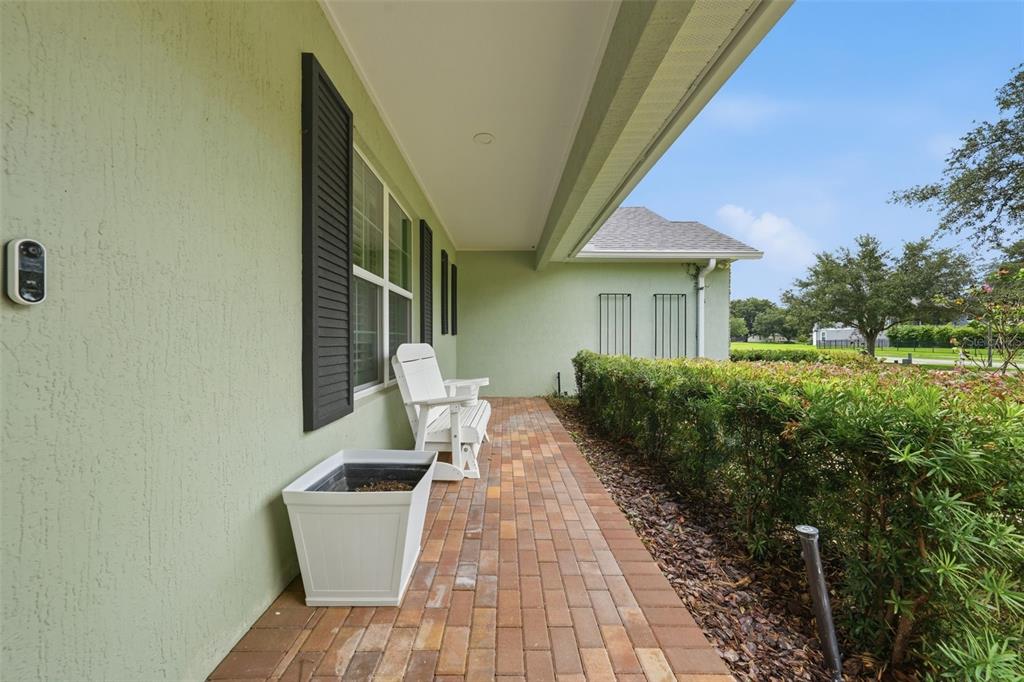 A covered brick porch features a white chair, a planter, and light green exterior walls — 4526 CLAIRE ROSE COURT, MOUNT DORA, FL
