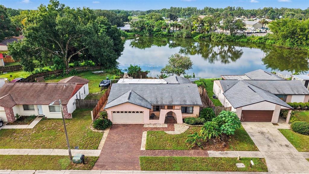 An aerial view shows a single-story house with a brick driveway facing a small lake — 21502 NORTHWOOD DRIVE, LUTZ, FL