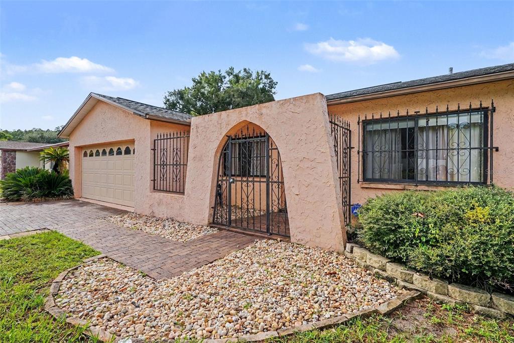 A peach-colored house exterior features a gated courtyard entrance, a garage, and security bars — 21502 NORTHWOOD DRIVE, LUTZ, FL