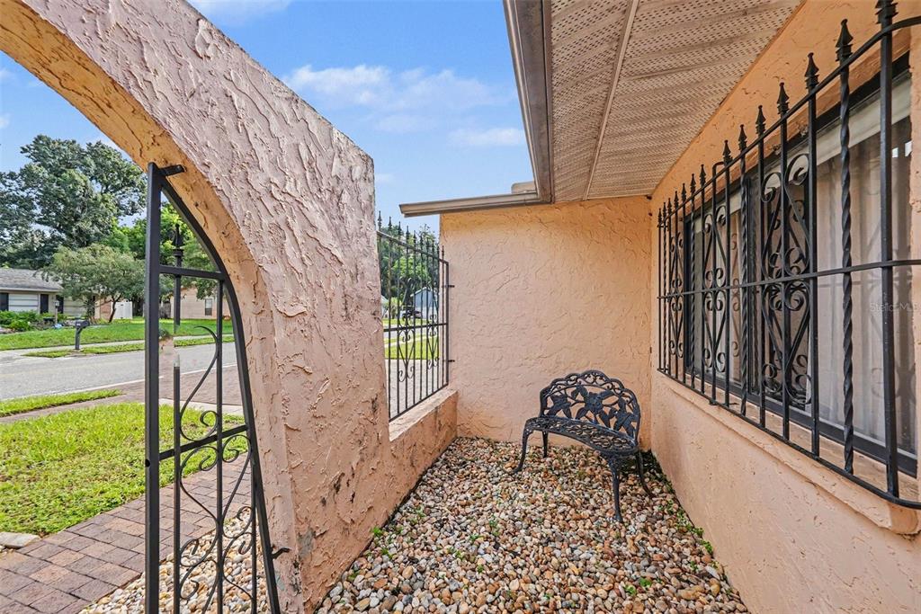 A small outdoor patio features a stone-covered floor, a metal bench, and decorative iron fencing — 21502 NORTHWOOD DRIVE, LUTZ, FL