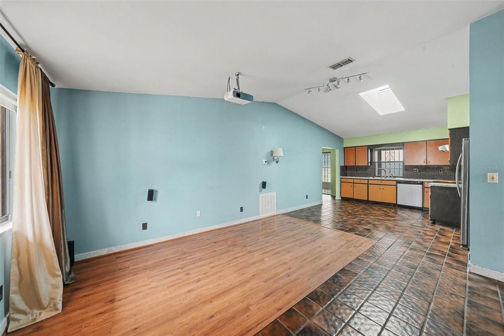 An open-concept living area with light blue walls, wood-look flooring, and an adjacent tiled kitchen — 21502 NORTHWOOD DRIVE, LUTZ, FL