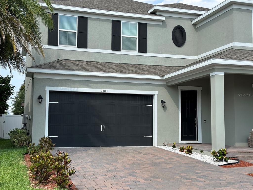 A two-story house exterior features a dark garage door, black shutters, and a paved driveway — 2403 BISCOTTO CIRCLE, DAVENPORT, FL
