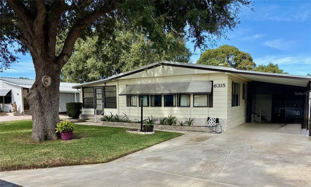 The exterior of a light-colored manufactured home features a brick planter and metal window awnings — 6315 GROVE POINTE DRIVE SE, WINTER HAVEN, FL