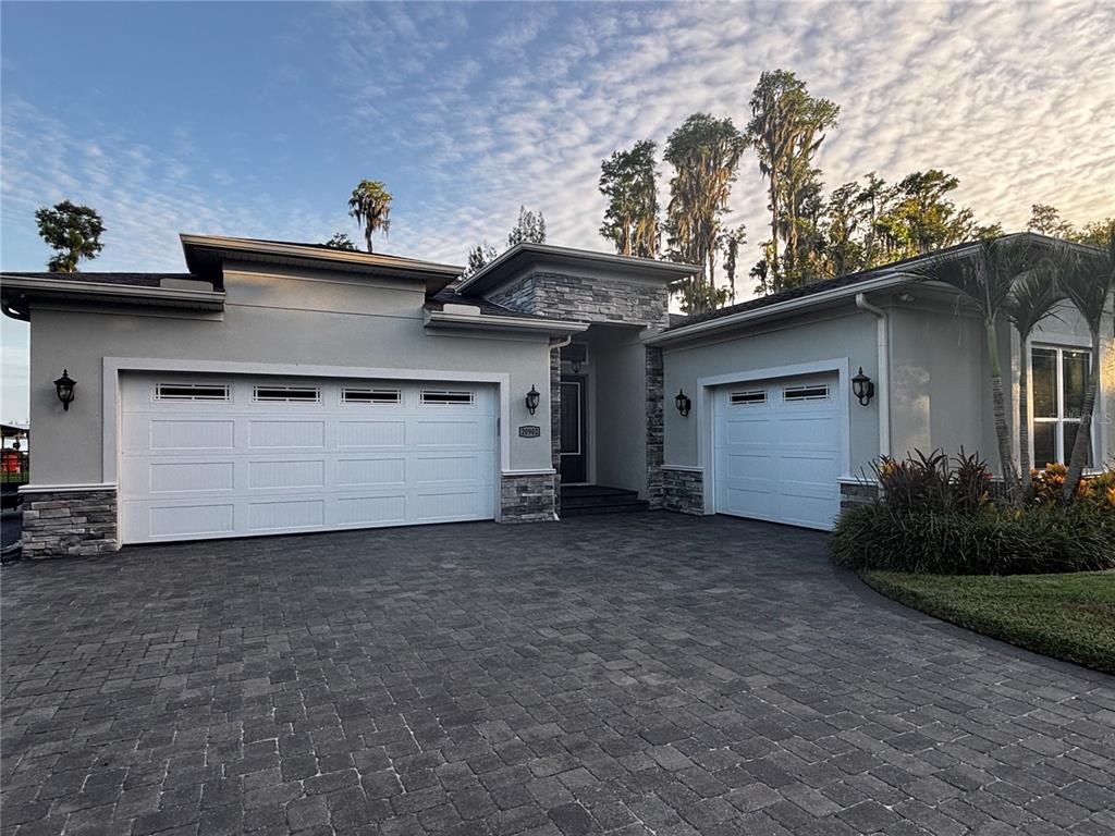 A single-story house exterior features a three-car garage, stone accents, and a paved driveway — 20902 RAGAN LANE, LAND O LAKES, FL