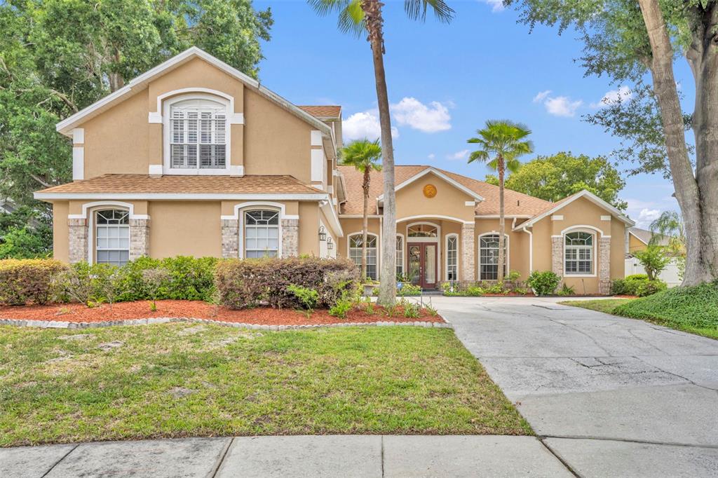 A two-story tan stucco house with a brick-accented facade and a concrete driveway — 2518 EMERALD TREE LANE, APOPKA, FL