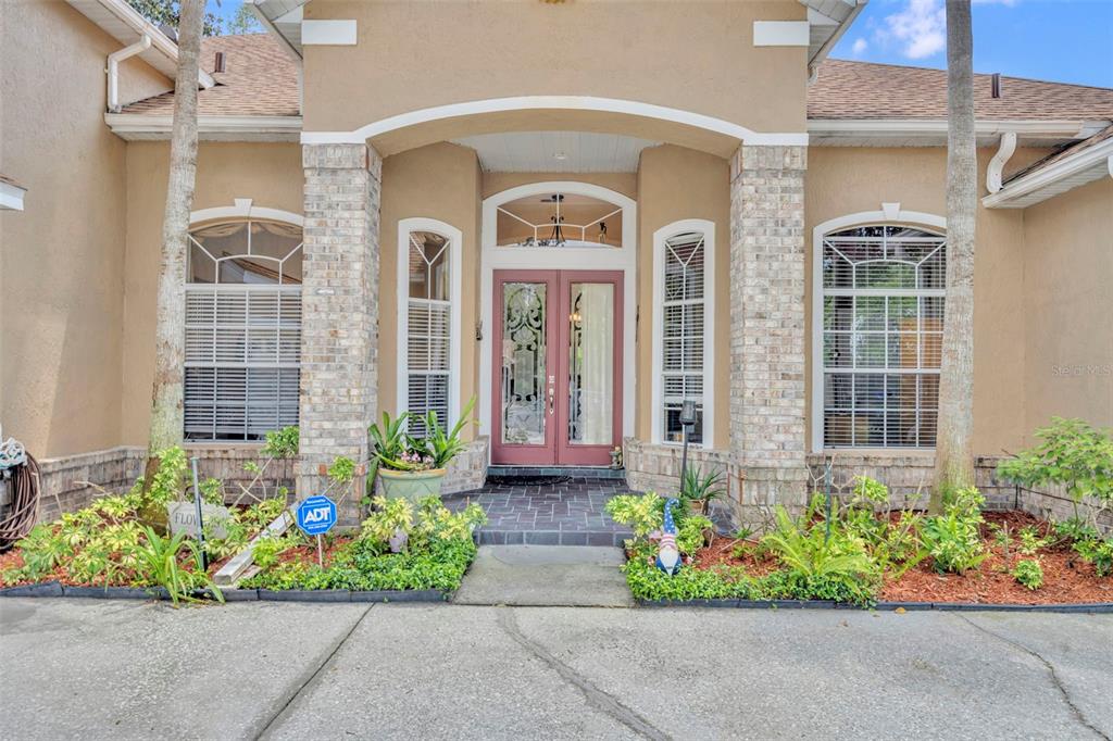 The exterior of a tan house features a brick-columned entryway with double glass doors — 2518 EMERALD TREE LANE, APOPKA, FL
