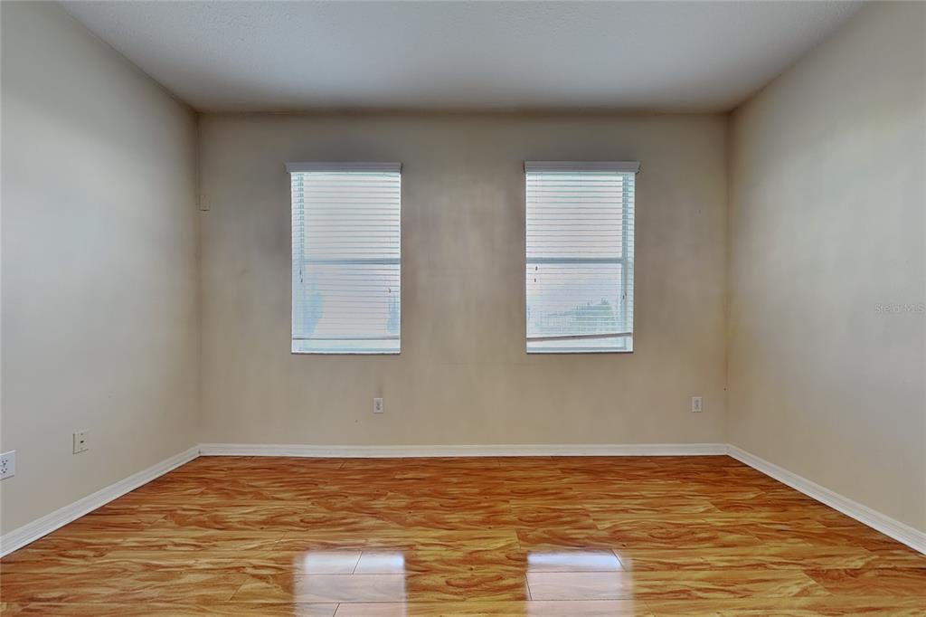 An empty room features light-colored walls, two windows with blinds, and wood-look laminate flooring — 9609 ROYAL FERN COURT, TAMPA, FL