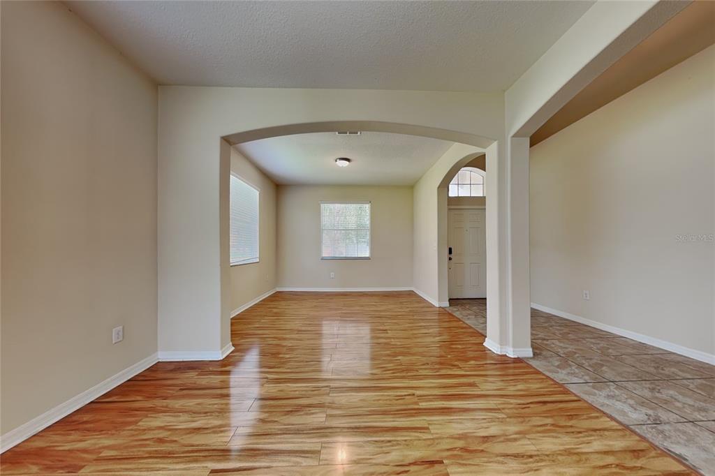 An empty room with wood-look flooring, an arched entryway, and a view of the front door — 9609 ROYAL FERN COURT, TAMPA, FL
