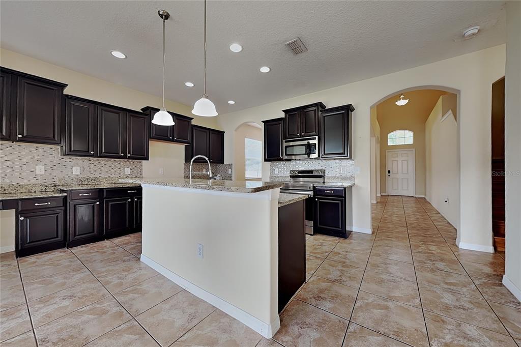 A kitchen features dark wood cabinets, granite countertops, tile flooring, and a central island — 9609 ROYAL FERN COURT, TAMPA, FL