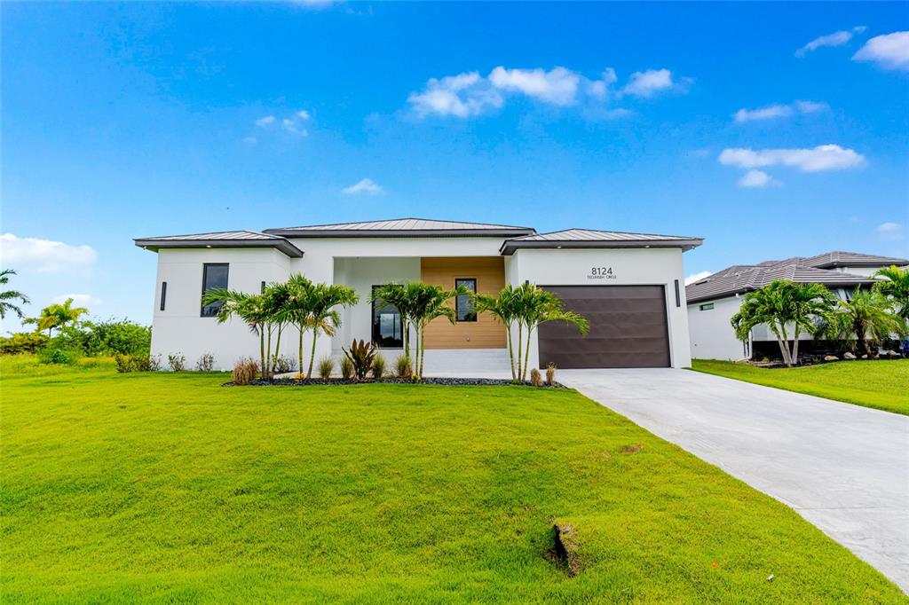 A modern, single-story white house with a brown garage door and palm trees in front — 8124 TECUMSEH CIRCLE, PORT CHARLOTTE, FL