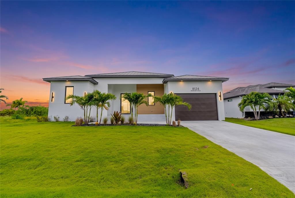 A modern single-story house with a white exterior, dark garage door, and palm trees — 8124 TECUMSEH CIRCLE, PORT CHARLOTTE, FL