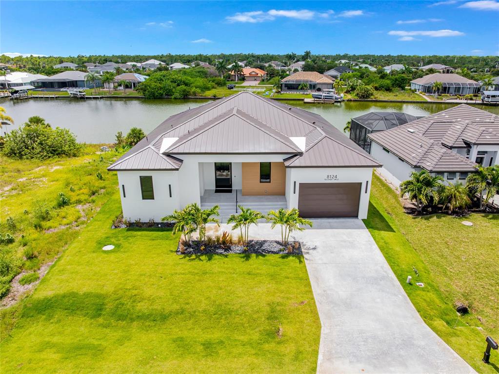 An aerial view of a modern single-story house with a metal roof and concrete driveway — 8124 TECUMSEH CIRCLE, PORT CHARLOTTE, FL