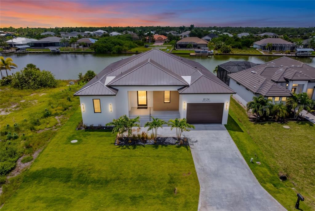 An aerial view of a modern single-story house with a metal roof and canal frontage — 8124 TECUMSEH CIRCLE, PORT CHARLOTTE, FL