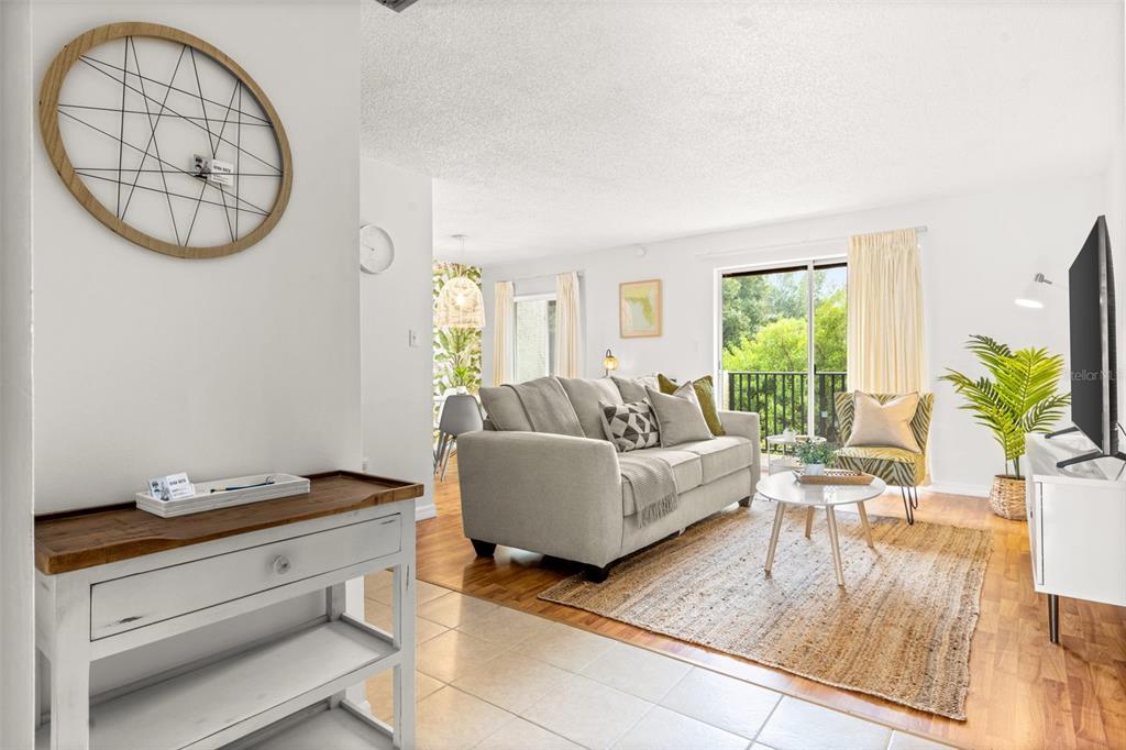 A bright living room features a beige sofa, a jute rug, and a wooden console — 4215 E BAY DRIVE UNIT 1806D, CLEARWATER, FL