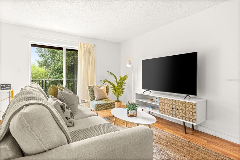 A living room features a grey sofa, a patterned media console, and a sliding glass door — 4215 E BAY DRIVE UNIT 1806D, CLEARWATER, FL