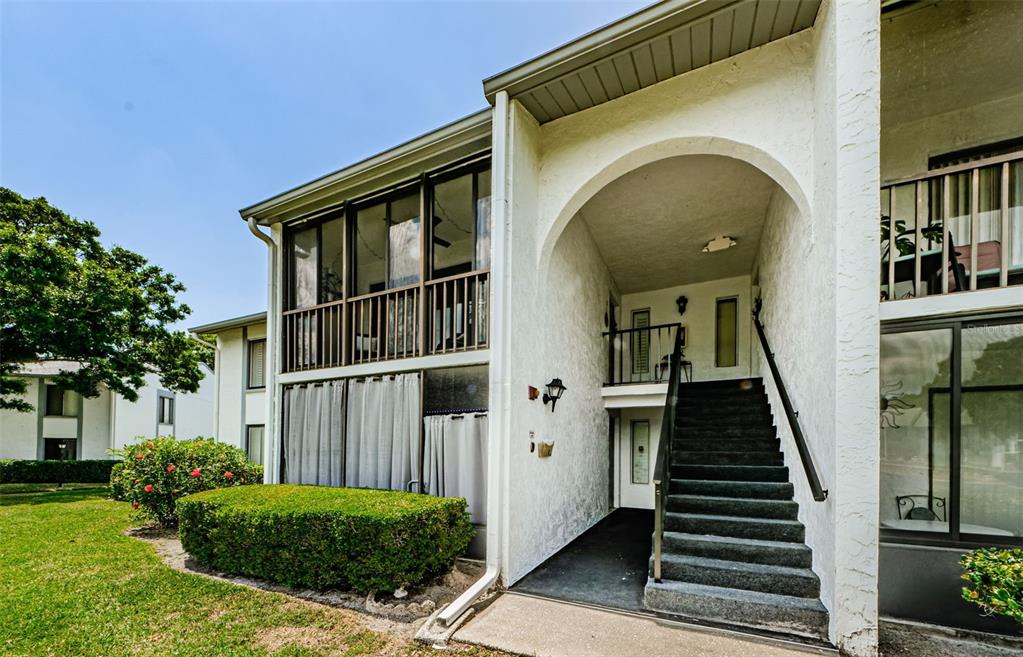An exterior view of a two-story apartment building featuring a covered staircase and screened balconies — 1151 PINE RIDGE CIRCLE W UNIT F1, TARPON SPRINGS, FL