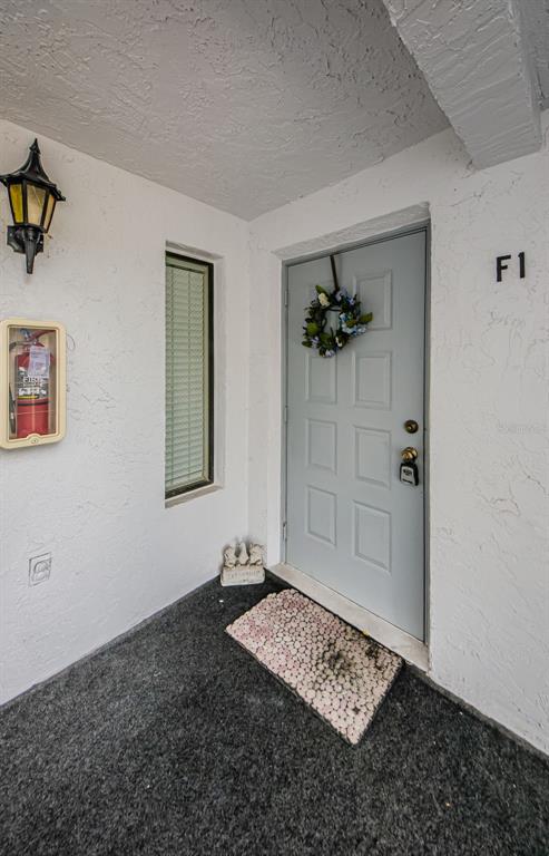 An exterior view of a residential entryway featuring a gray door, a wreath, and a fire extinguisher — 1151 PINE RIDGE CIRCLE W UNIT F1, TARPON SPRINGS, FL