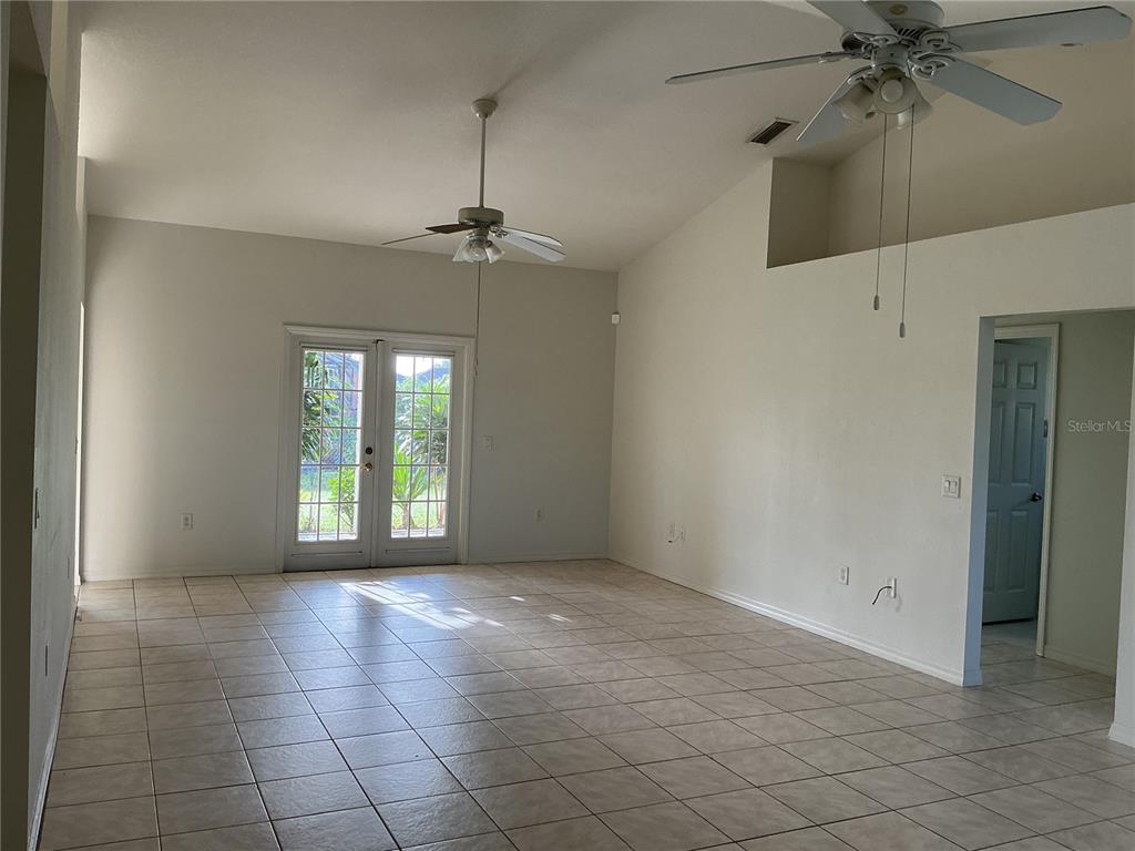 An empty living room with vaulted ceilings, tile flooring, two ceiling fans, and glass doors — 2700 S BISCAYNE DRIVE, NORTH PORT, FL