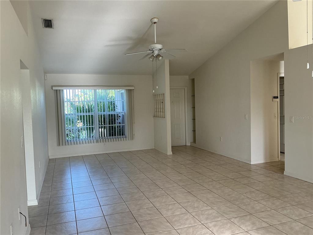 An empty living room with vaulted ceilings, tile flooring, and a large window with blinds — 2700 S BISCAYNE DRIVE, NORTH PORT, FL