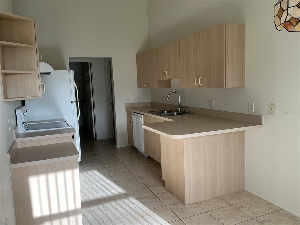 A kitchen features light wood cabinets, tan laminate countertops, tile flooring, and a white refrigerator — 2700 S BISCAYNE DRIVE, NORTH PORT, FL