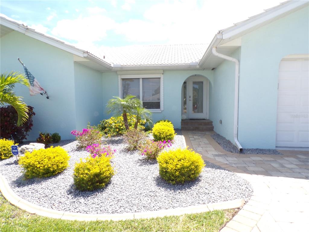 A light blue house exterior features a stone walkway, a front door, and landscaped garden beds — 3804 TURTLE DOVE BOULEVARD, PUNTA GORDA, FL
