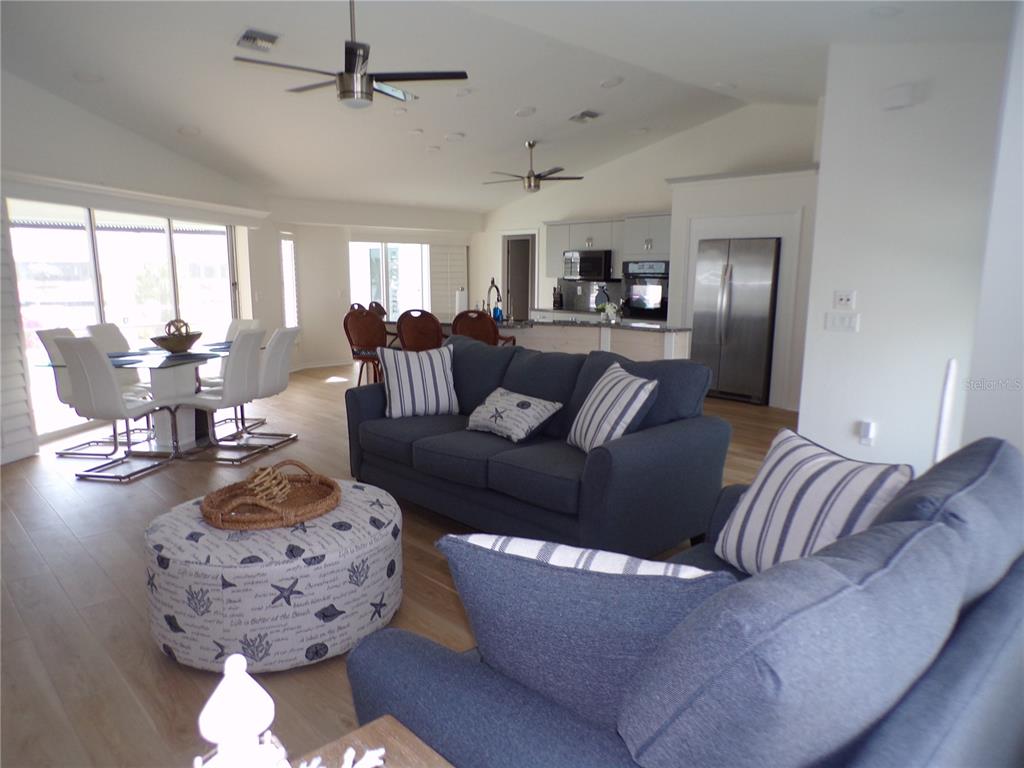 An open-concept living room features a blue sofa, a patterned ottoman, and a dining area — 3804 TURTLE DOVE BOULEVARD, PUNTA GORDA, FL