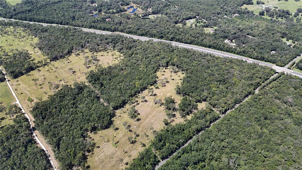 An aerial view shows a large, partially cleared wooded lot bordered by a highway — WOH #1 (15ac) NW 193RD ST, MICANOPY, FL