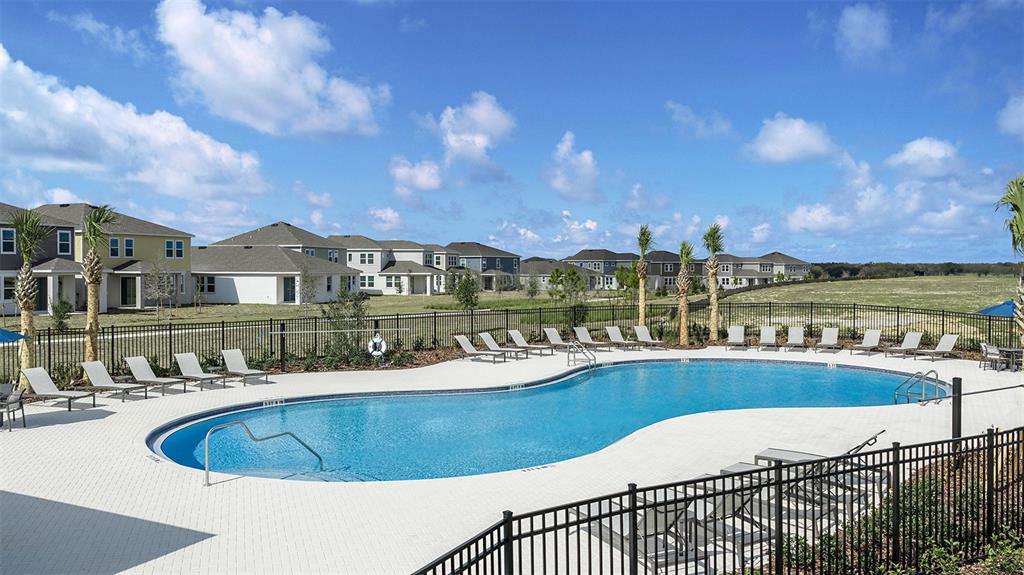 A swimming pool with lounge chairs sits in front of a residential neighborhood under blue skies — 7760 CLOUDBURST DRIVE, GROVELAND, FL