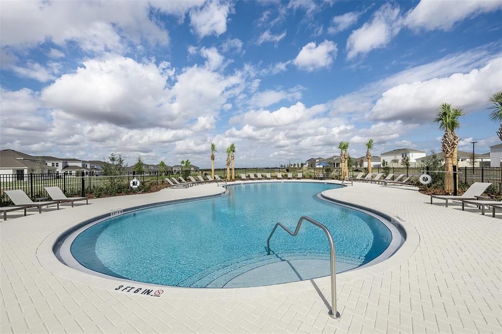 A community swimming pool with lounge chairs and palm trees under a cloudy sky — 7760 CLOUDBURST DRIVE, GROVELAND, FL