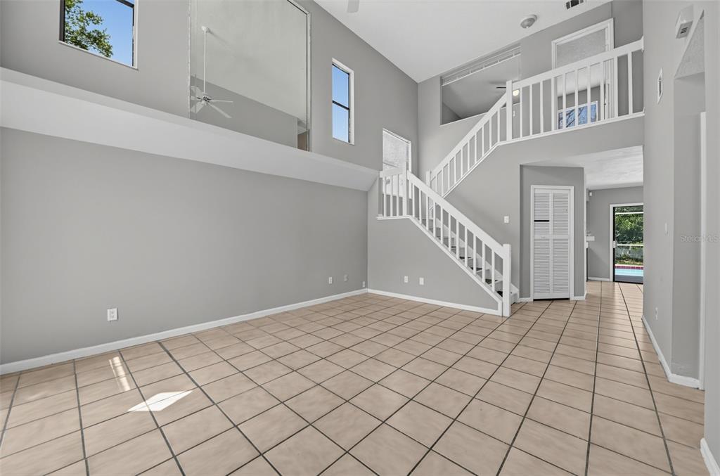 An empty living room features high ceilings, tiled floors, and a staircase with white railings — 4226 CLOVERLEAF PLACE, CASSELBERRY, FL
