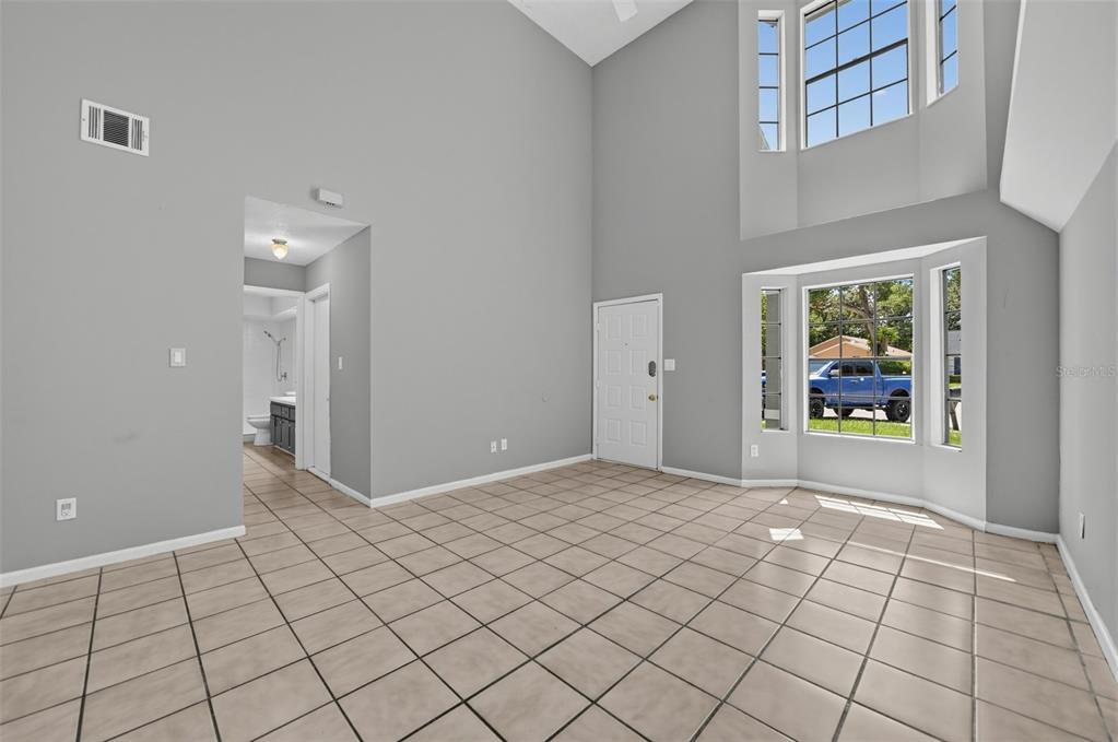 A high-ceilinged living room features light gray walls, beige tiled flooring, and a bay window — 4226 CLOVERLEAF PLACE, CASSELBERRY, FL