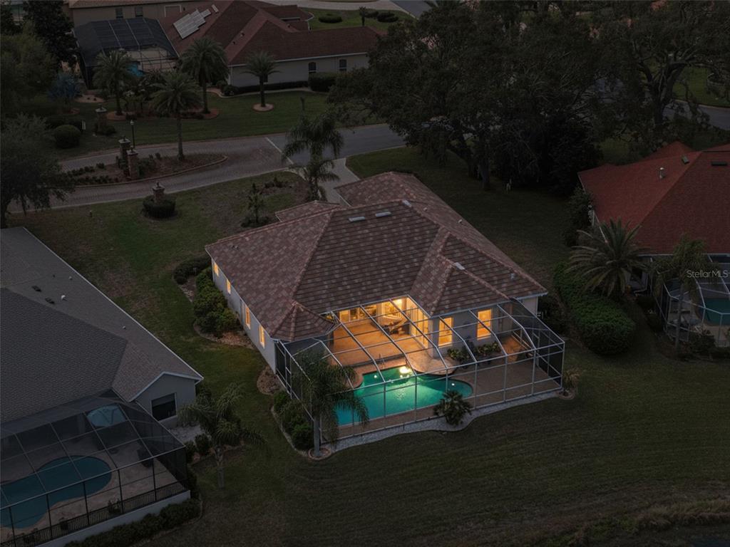 An aerial view of a house with a screened-in pool and patio at dusk — 9203 LAKE CYPRESS LOOP, WEEKI WACHEE, FL
