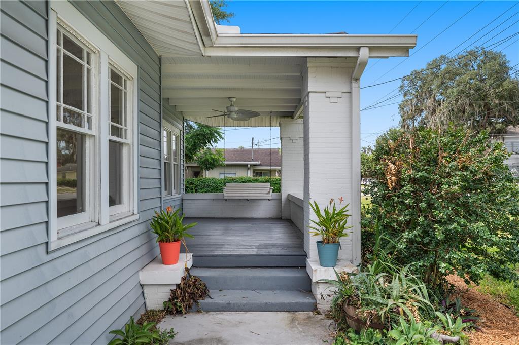 A covered front porch features a hanging swing, gray wooden decking, and two potted plants — 816 S INGRAHAM AVENUE, LAKELAND, FL