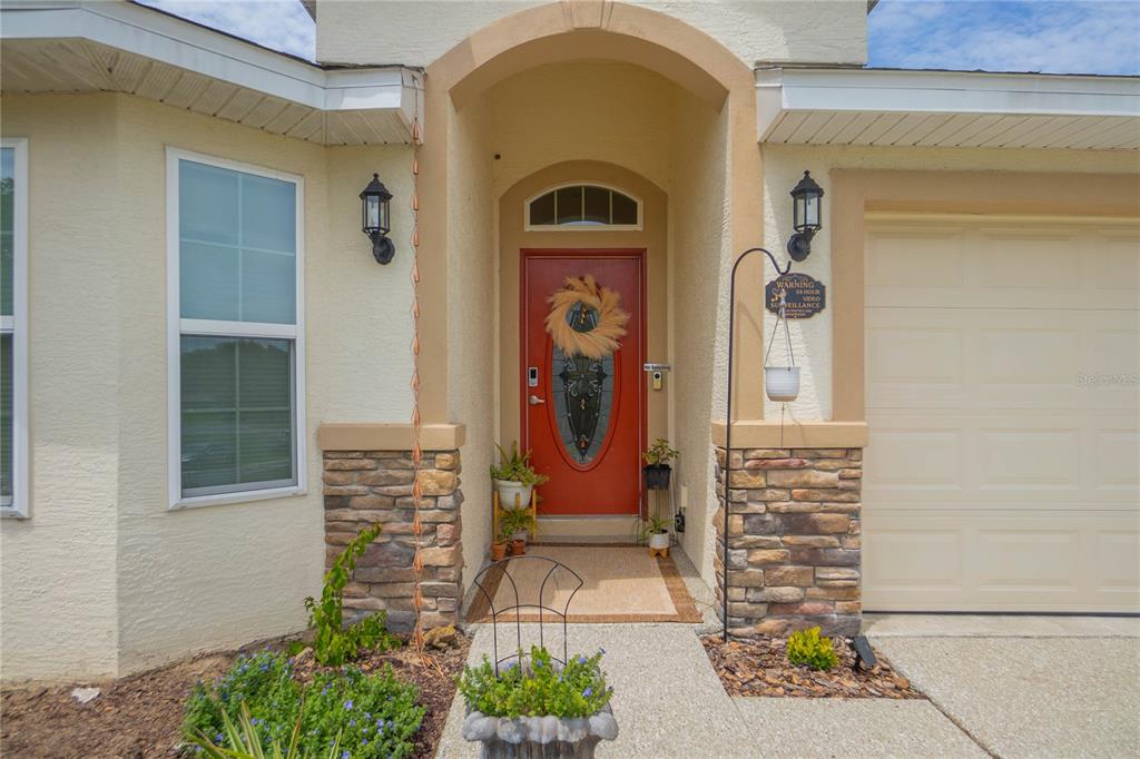 The exterior of a house features a red front door, stone accents, and a garage — 3271 N BURROUGHS PATH, BEVERLY HILLS, FL
